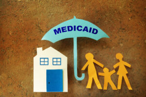 Paper cutout family with house under a Medicaid umbrella                               